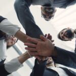 Dynamic low-angle shot of a diverse business team joining hands in unity within a bright, modern office.
